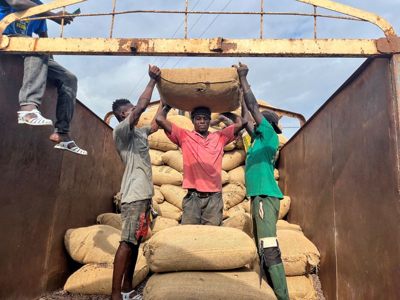 Workers help their colleague to carry a bag of cocoa beans on his head in San-Pedro